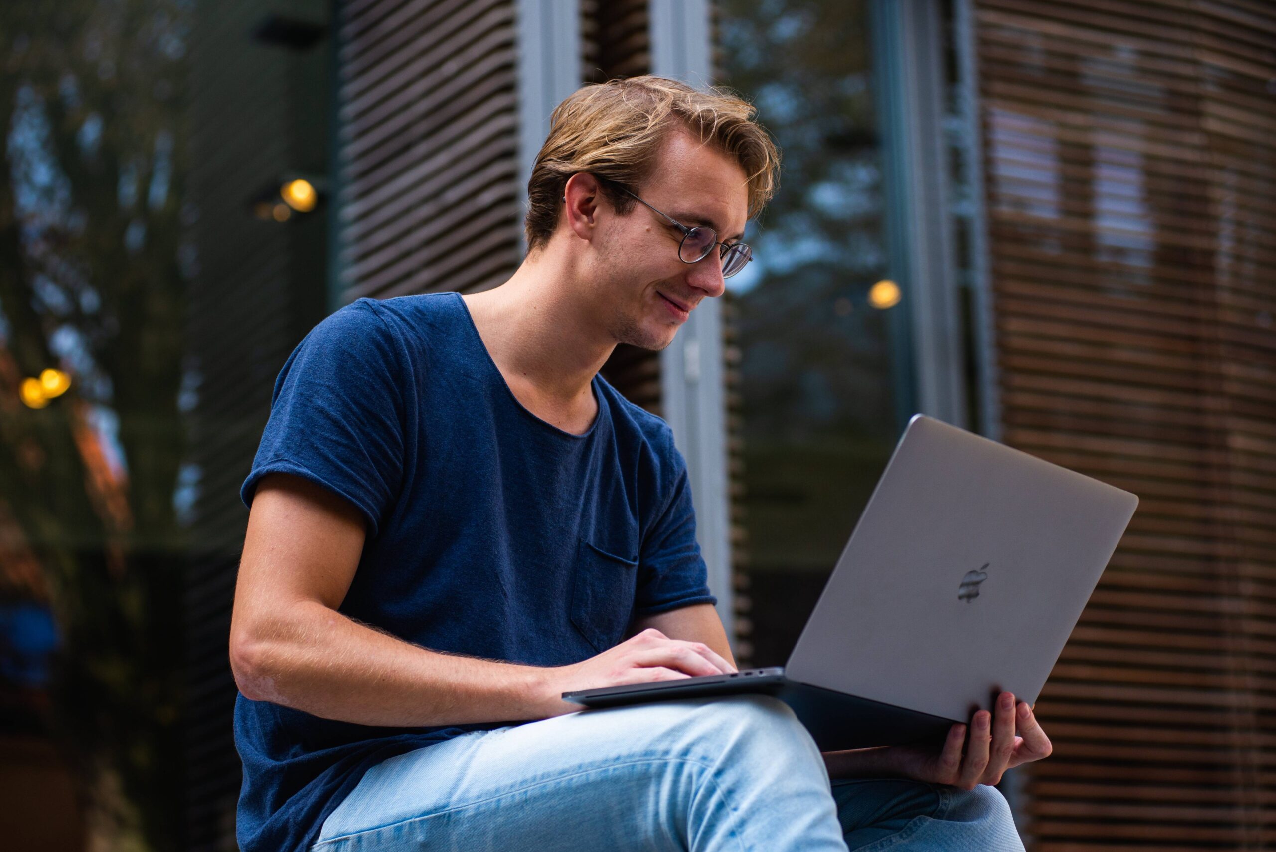 A focused man on a bench, using a laptop to work while enjoying the outdoors.